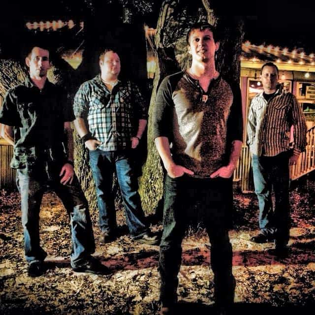 Four guys standing in front of a tree.