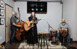 Three people stand around in the living room playing their instruments.