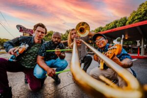 members Of Good Nature pose in front of building holding instruments